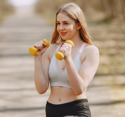 Fit woman lifting dumbbells on a sunny day, embracing a healthy outdoor workout.