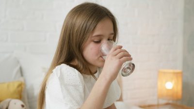 A young girl drinks water in a cozy bedroom, highlighting hydration and comfort.